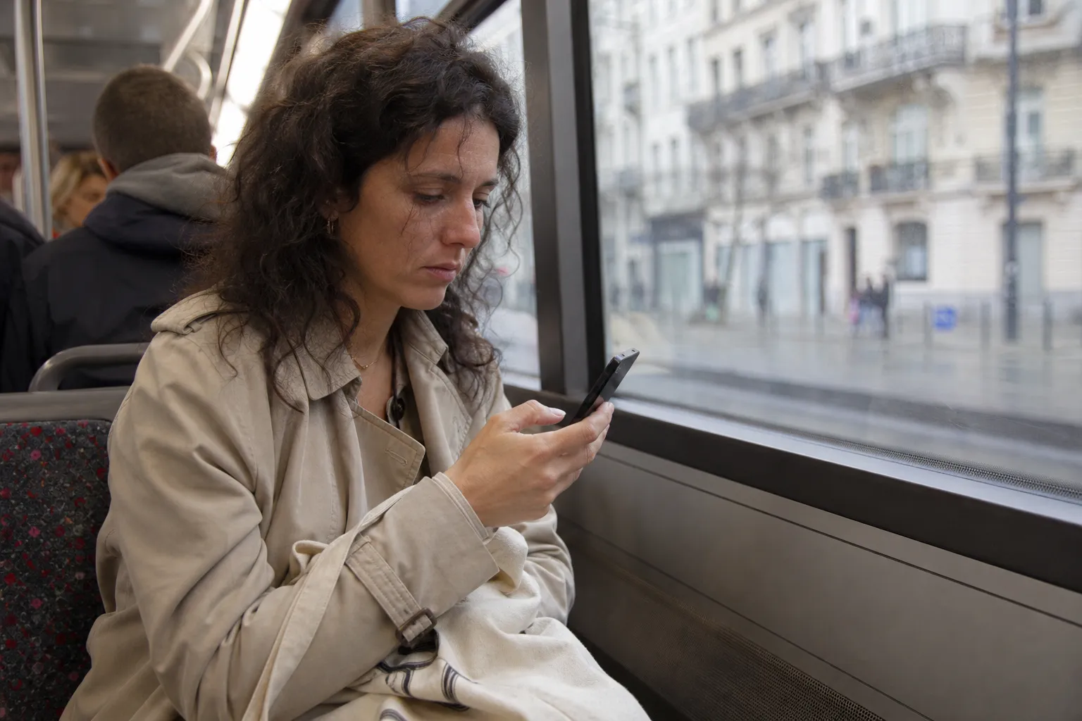 Une femme d'une trentaine d'années fait défiler son téléphone, assise près de la fenêtre d'un tram à Bruxelles.
